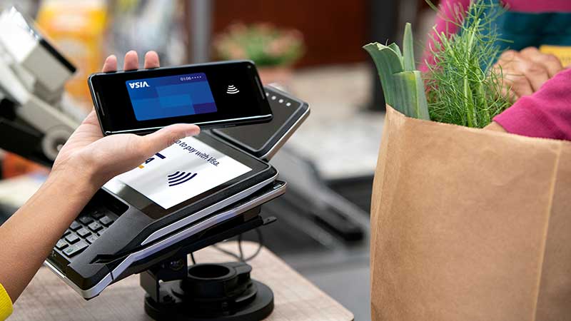 Paying for a bag of groceries by holding a smartphone up to a contactless reader.